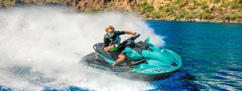 Homem pilotando jet-ski azul da Kawasaki em alta velocidade na água