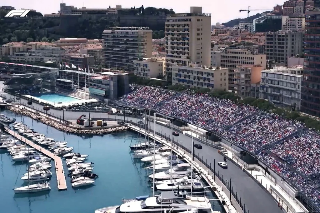 Vista da marina de Monte Carlo durante o GP de Mônaco, com arquibancadas do circuito e embarcações atracadas ao lado da pista.