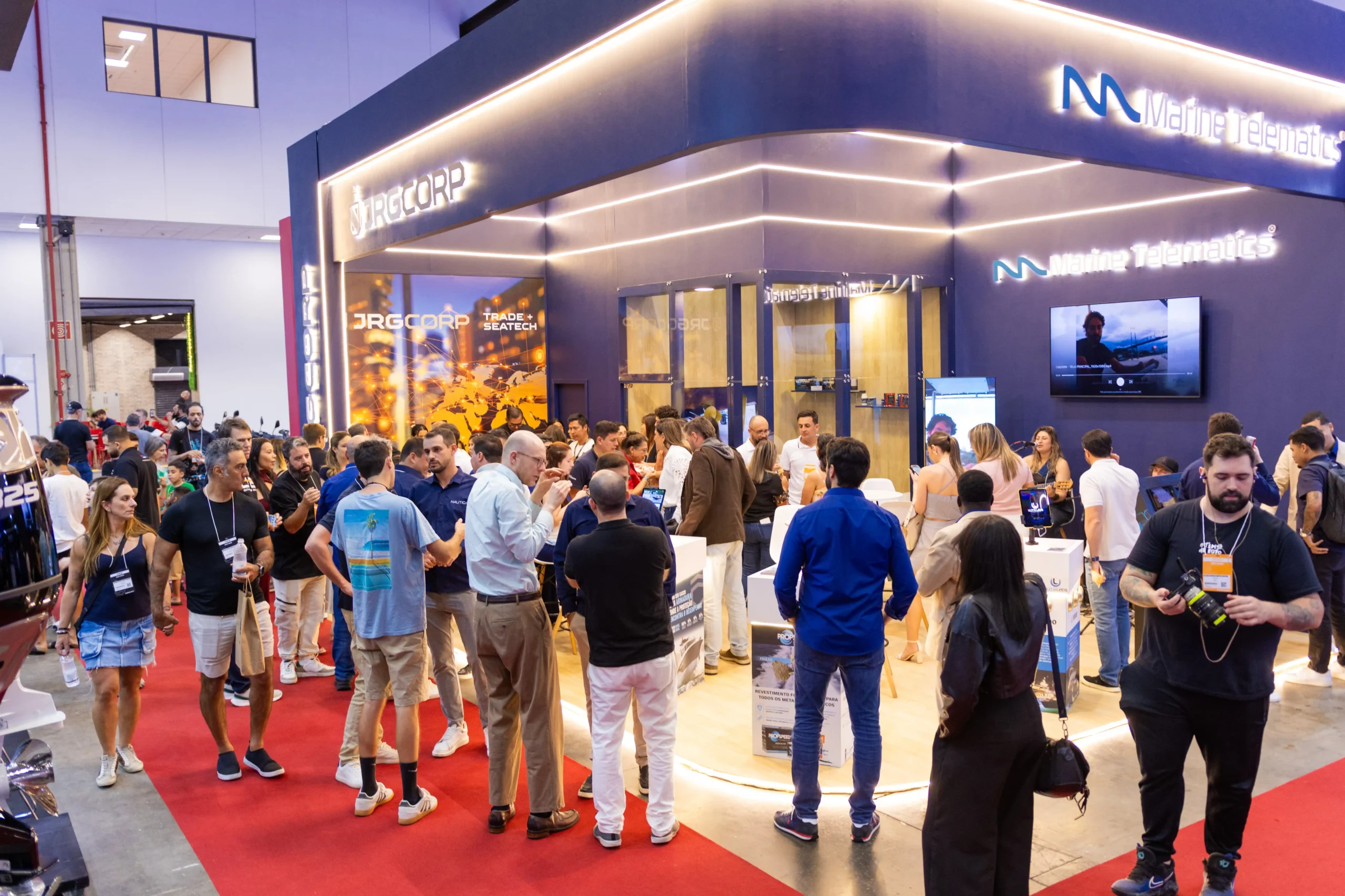 Estande da Marine Telematics e JRGCORP no São Paulo Boat Show com visitantes conhecendo tecnologias de comando eletrônico e telemetria para embarcações.