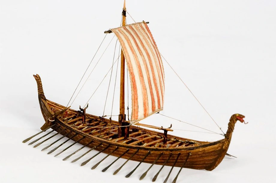 Modelo em miniatura de um navio viking com vela listrada e remos.
