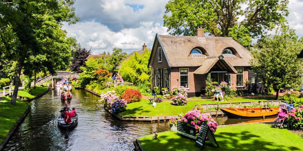 Canais de Giethoorn com barcos, flores e casa tradicional de telhado de palha na Holanda.