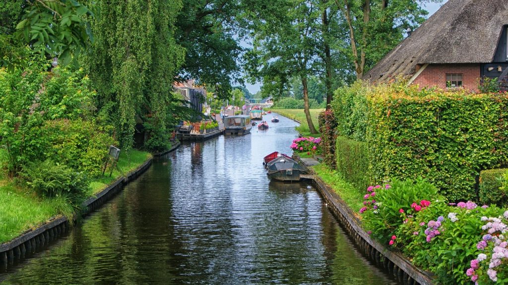 Canal de Giethoorn cercado por vegetação, flores, barcos e casas tradicionais na Holanda.