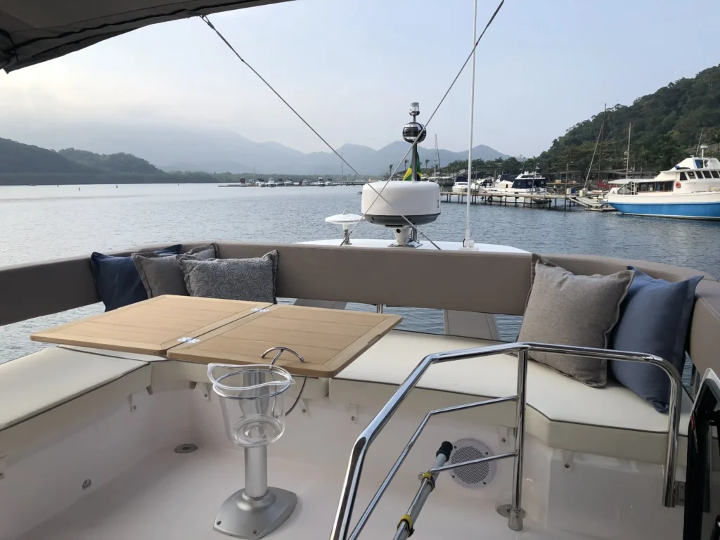 Flybridge da Sessa F42 com bancos estofados, mesa de madeira e vista para a água e as montanhas.