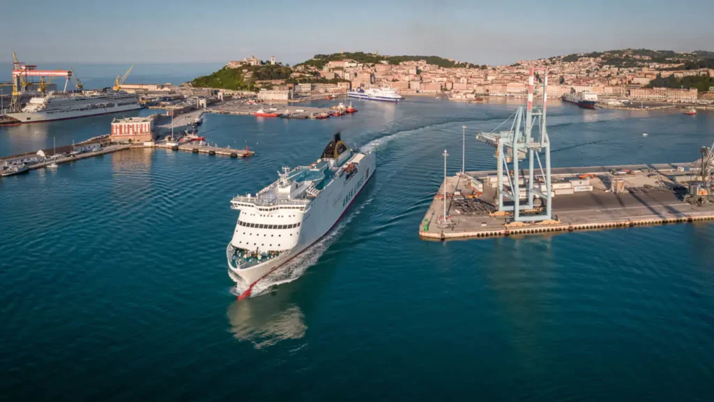 Porto de Ancona, na Itália, com navio de passageiros navegando entre os terminais portuários.